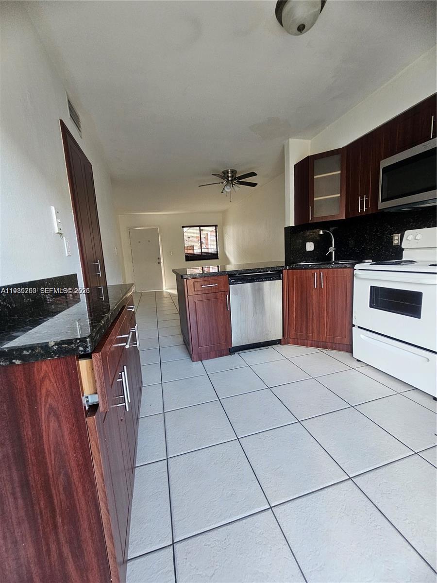 A kitchen features dark wood cabinets, black granite countertops, and white tile flooring — 5460 W 21st CT # 310, Hialeah FL 33016, HIALEAH, FL