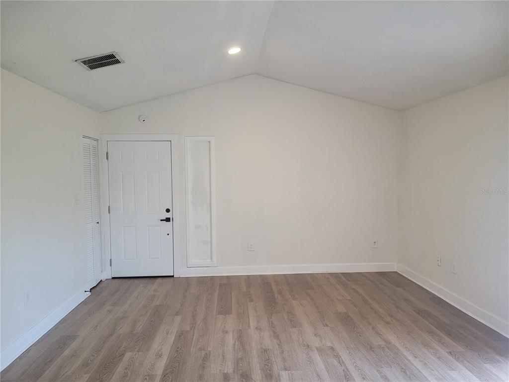 An empty room features white walls, a vaulted ceiling, and light-toned wood-look flooring — 1236 DOVEHILL DRIVE UNIT 1248, APOPKA, FL
