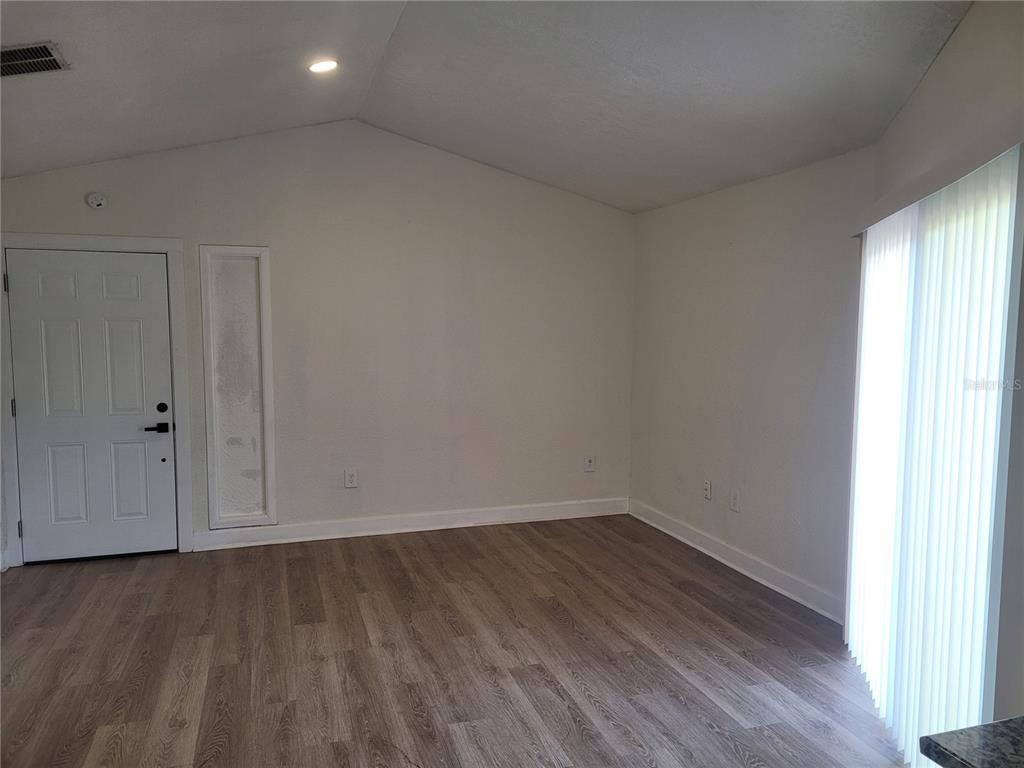 An empty room features light wood-look flooring, white walls, a vaulted ceiling, and a sliding door — 1236 DOVEHILL DRIVE UNIT 1248, APOPKA, FL