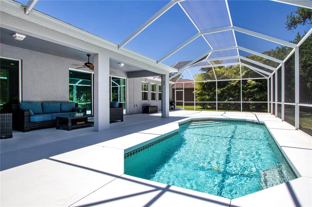 A covered patio with a blue sofa overlooks a swimming pool inside a screened enclosure — 5001 65TH TERRACE E, ELLENTON, FL