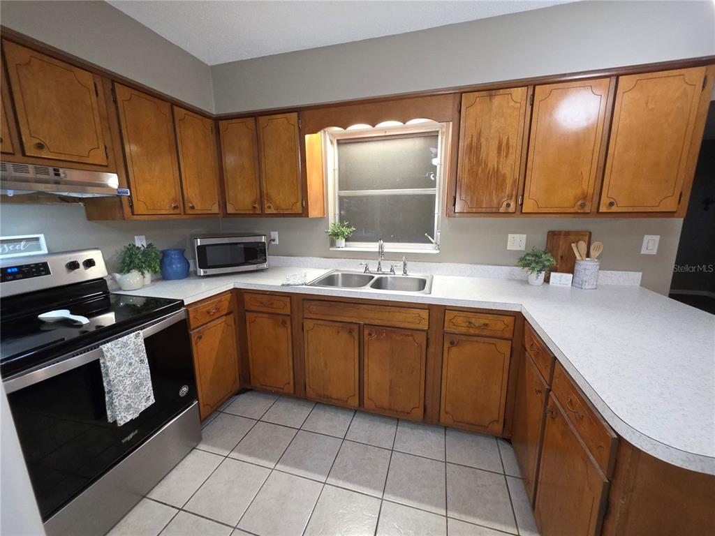 A kitchen features wood cabinets, a stainless steel stove, a double sink, and tiled floors — 21654 SW RAINTREE STREET, DUNNELLON, FL