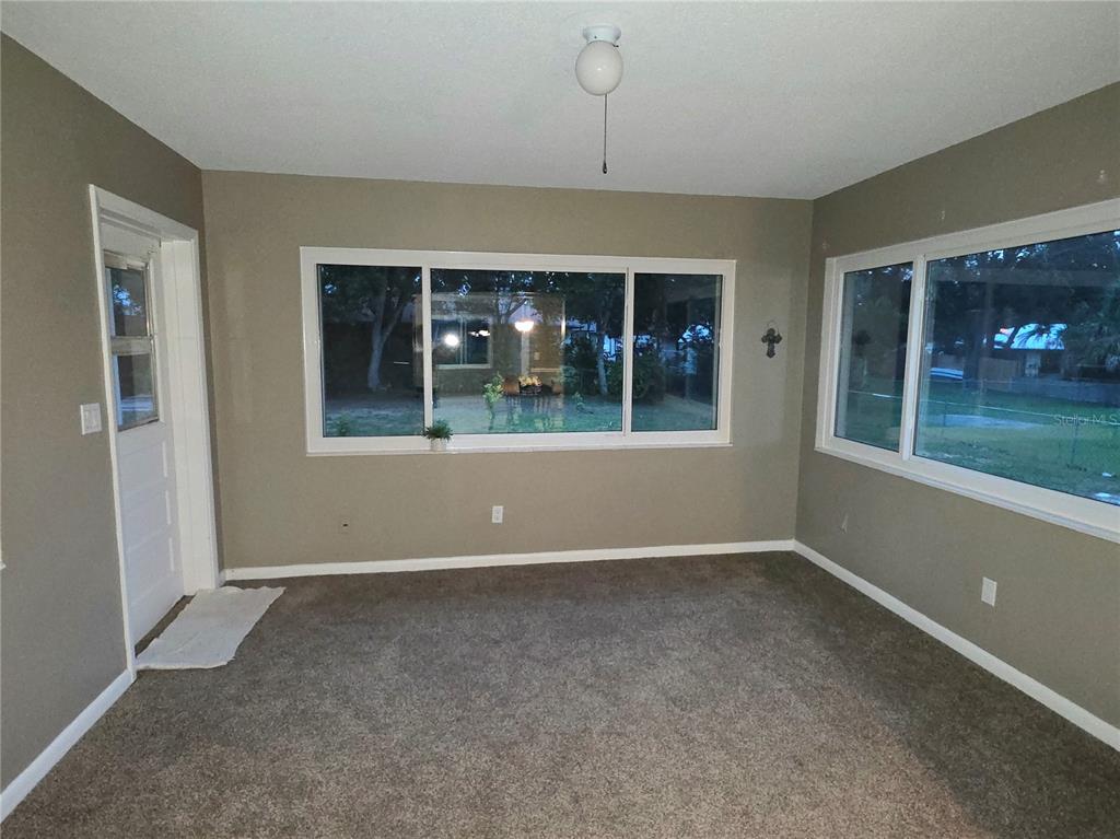 A room with gray walls, brown carpet, and large windows looking out to a yard — 21654 SW RAINTREE STREET, DUNNELLON, FL