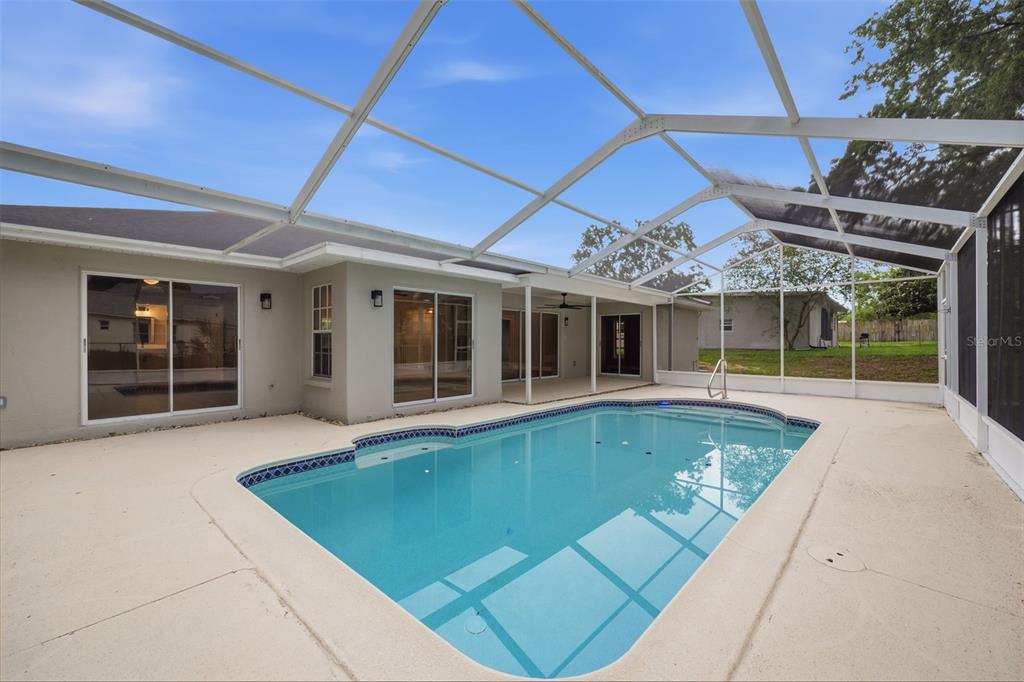 A swimming pool sits on a concrete patio enclosed by a screened-in lanai — 2489 AMHERST AVENUE, SPRING HILL, FL