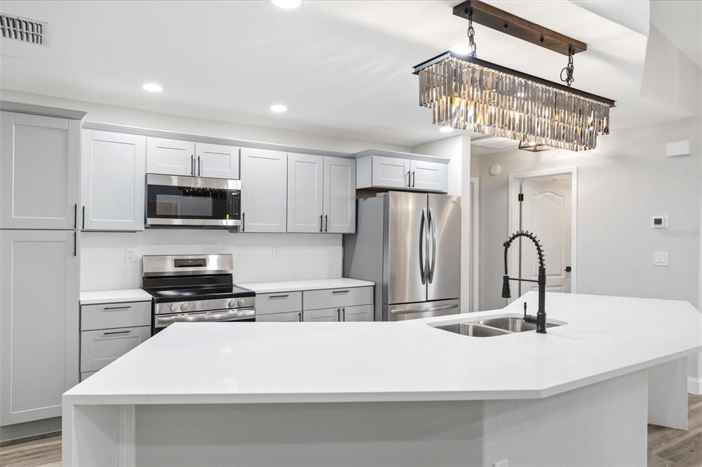 A modern kitchen features light gray cabinets, stainless steel appliances, and a white quartz island — 2489 AMHERST AVENUE, SPRING HILL, FL
