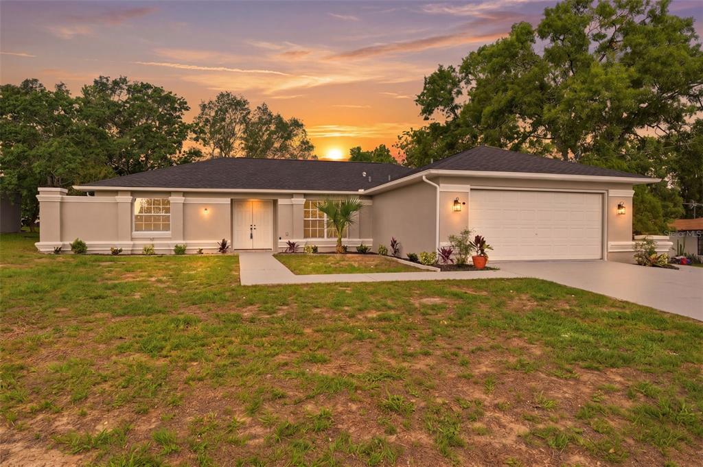 A single-story house with a white garage and double front doors at sunset — 2489 AMHERST AVENUE, SPRING HILL, FL