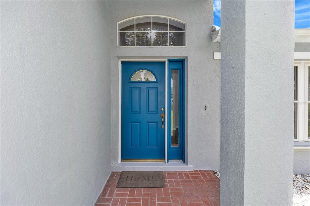 A blue front door with a sidelight and arched transom sits on a brick porch — 17020 WOODCREST WAY, CLERMONT, FL