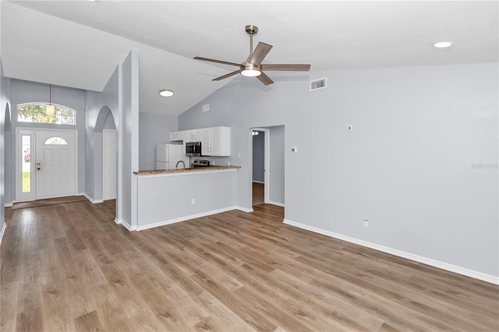 An open-concept living area features light gray walls, wood-look flooring, and a kitchen pass-through — 17020 WOODCREST WAY, CLERMONT, FL