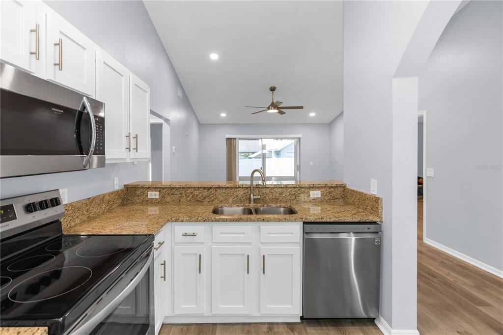 A kitchen with white cabinets, granite countertops, stainless steel appliances, and a view of the living area — 17020 WOODCREST WAY, CLERMONT, FL