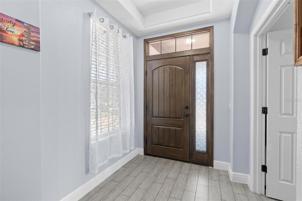 An entryway features a wood front door, a window with white curtains, and gray flooring — 1204 LEXINGTON AVENUE, DAVENPORT, FL