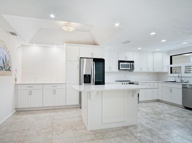 A bright white kitchen features a central island with woven bar stools and stainless appliances — 6081 SE Landing Way # 6, Stuart FL 34997, STUART, FL