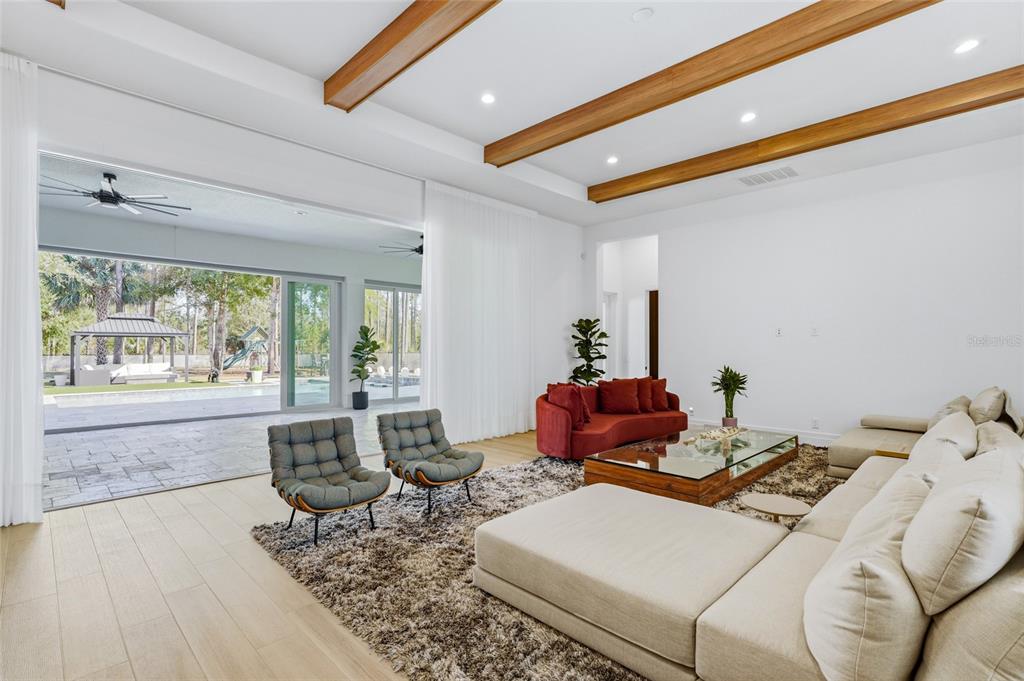 A modern living room features wood ceiling beams, a large sectional, and sliding glass doors — 16848 VINCI WAY, BELLA COLLINA, FL