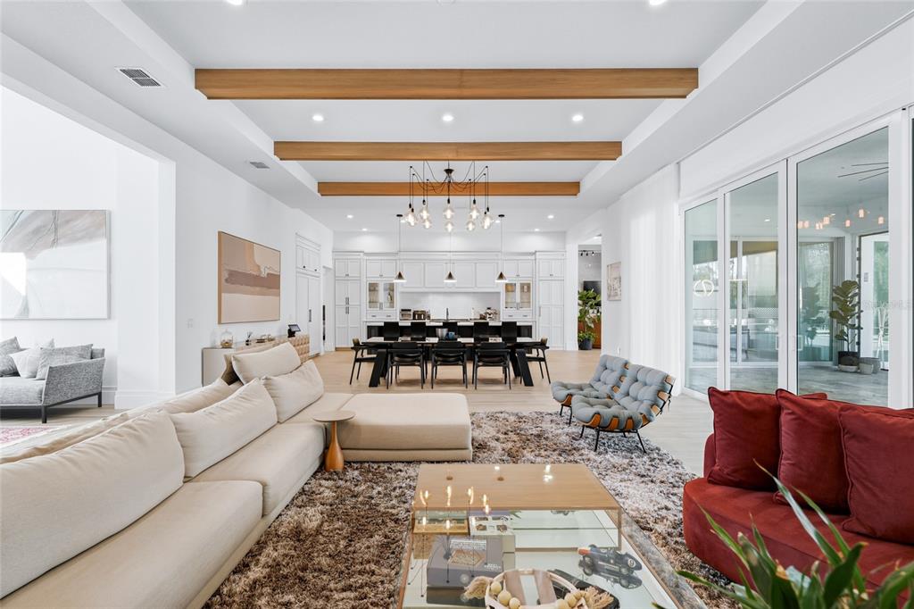 A spacious open-concept living room and kitchen featuring wood ceiling beams and modern furnishings — 16848 VINCI WAY, BELLA COLLINA, FL