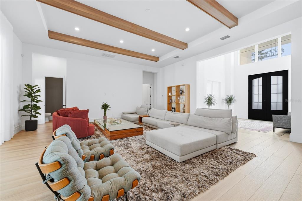 A spacious living room features white walls, wood ceiling beams, and a large area rug — 16848 VINCI WAY, BELLA COLLINA, FL