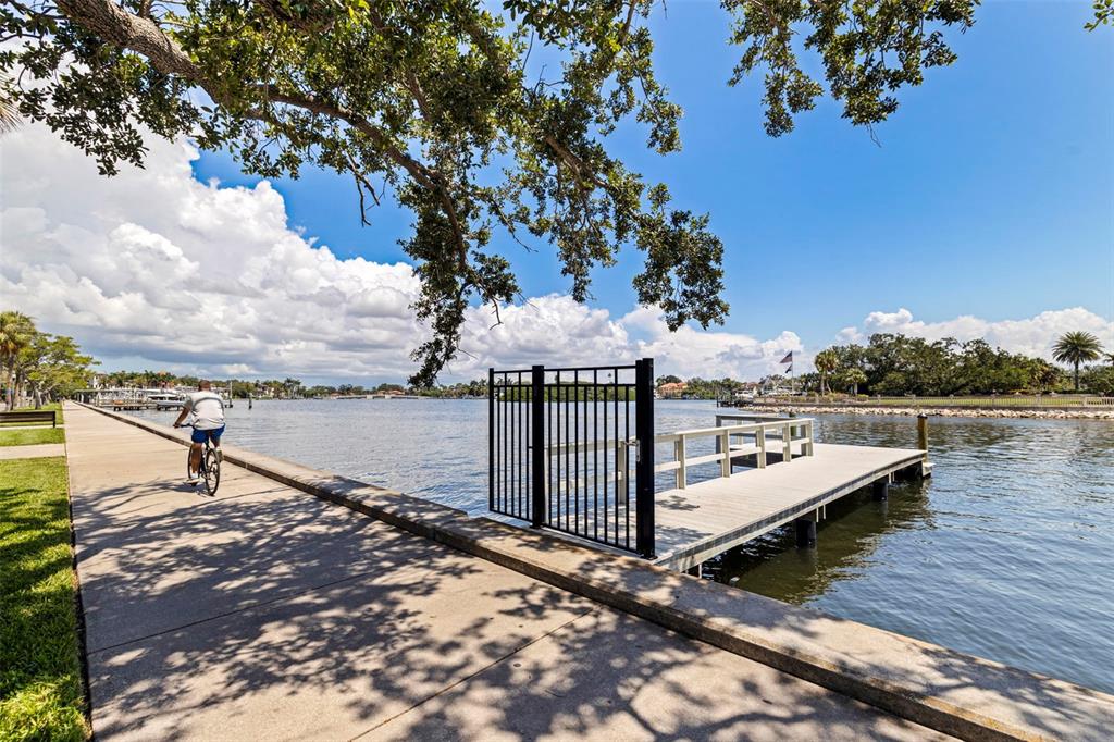 A person rides a bicycle along a concrete waterfront path next to a wooden dock — 1846 COFFEE POT BOULEVARD NE, ST PETERSBURG, FL