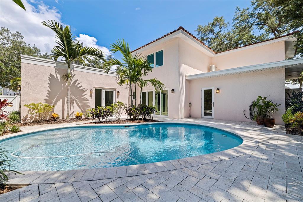 A light-colored house exterior features a swimming pool and patio surrounded by palm trees — 1846 COFFEE POT BOULEVARD NE, ST PETERSBURG, FL