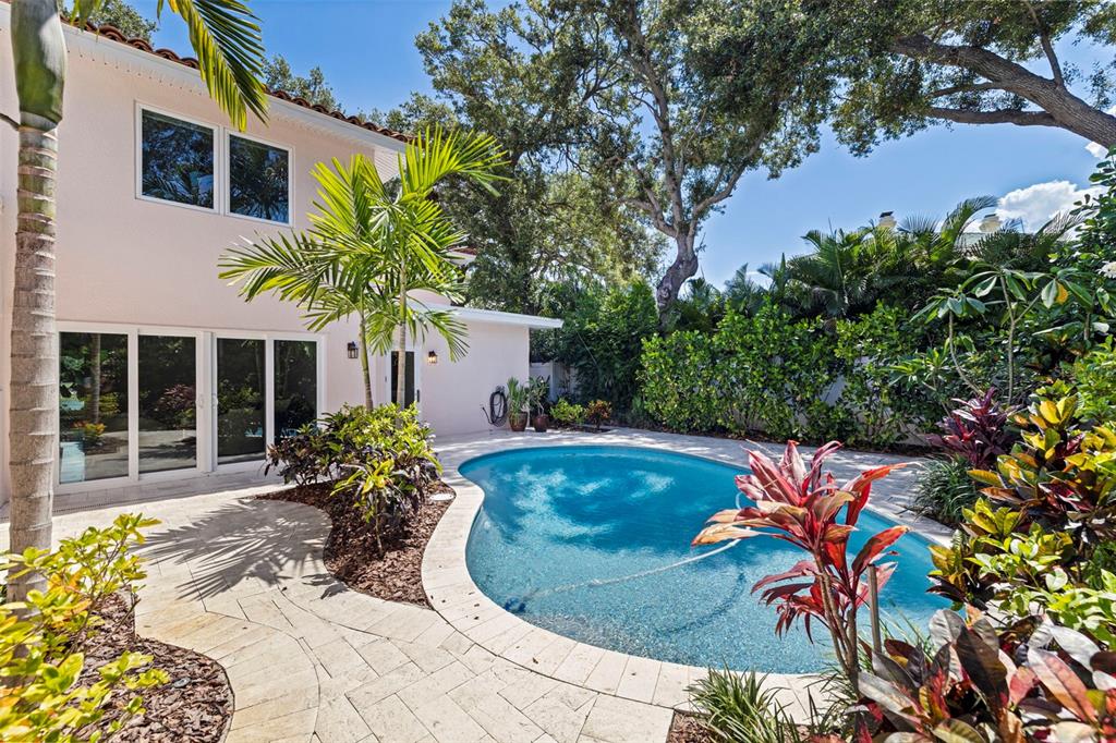 A backyard features a kidney-shaped swimming pool, stone patio, and lush tropical landscaping — 1846 COFFEE POT BOULEVARD NE, ST PETERSBURG, FL