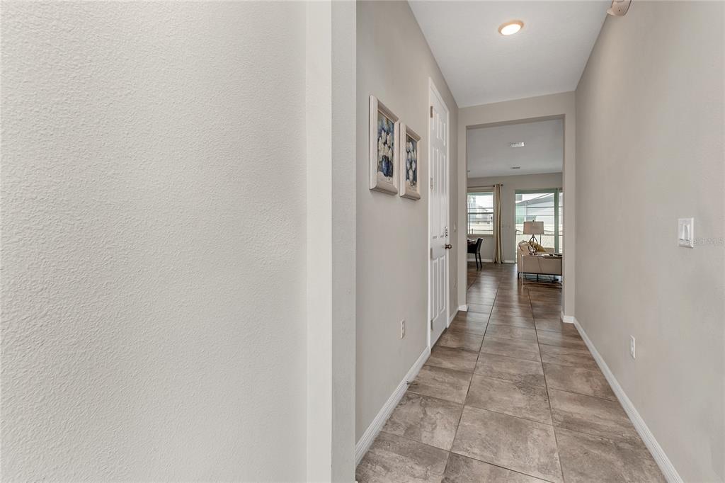 A hallway with light-colored walls and tile flooring leads toward an open living area — 9029 FLAMINGO KEY WAY, KISSIMMEE, FL