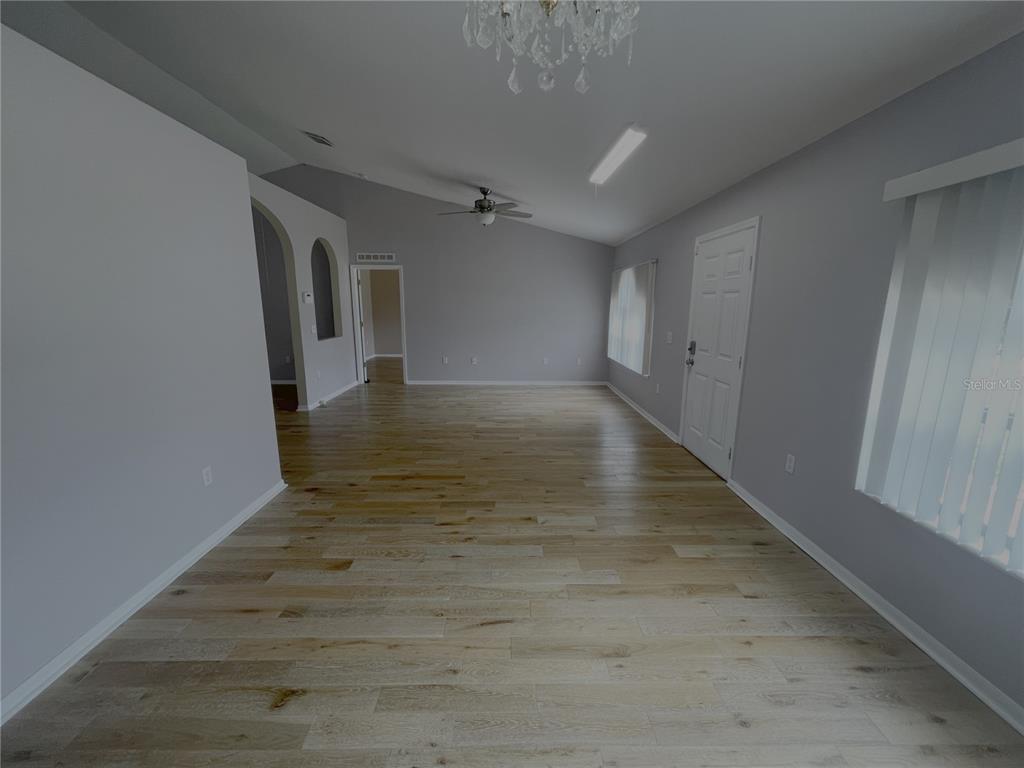 An empty living room features light wood-look flooring, gray walls, a ceiling fan, and a chandelier — 4535 SW 42ND STREET, OCALA, FL