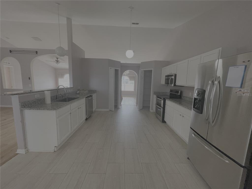 A kitchen with white cabinets, granite countertops, stainless steel appliances, and light-colored tile flooring — 4535 SW 42ND STREET, OCALA, FL