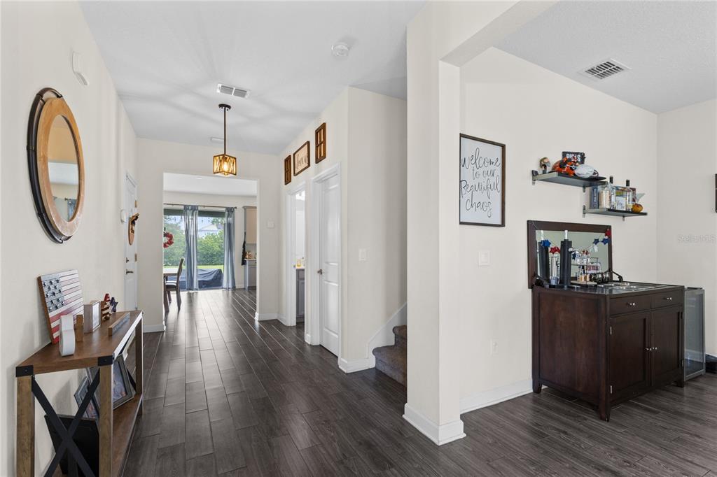 A hallway with dark wood-look tile flooring leads toward a bright room with sliding doors — 12016 FICTION AVENUE, ORLANDO, FL