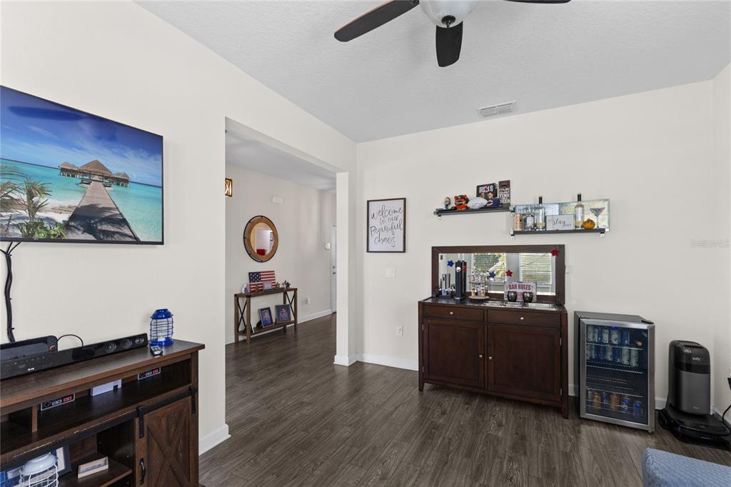 A living room features dark wood-look flooring, a television, a bar cabinet, and a ceiling fan — 12016 FICTION AVENUE, ORLANDO, FL