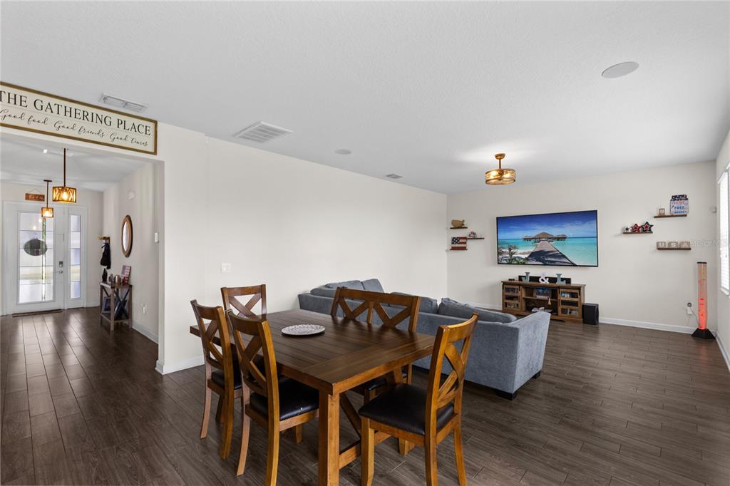 An open-concept living and dining area features dark wood flooring, a grey sofa, and a television — 12016 FICTION AVENUE, ORLANDO, FL