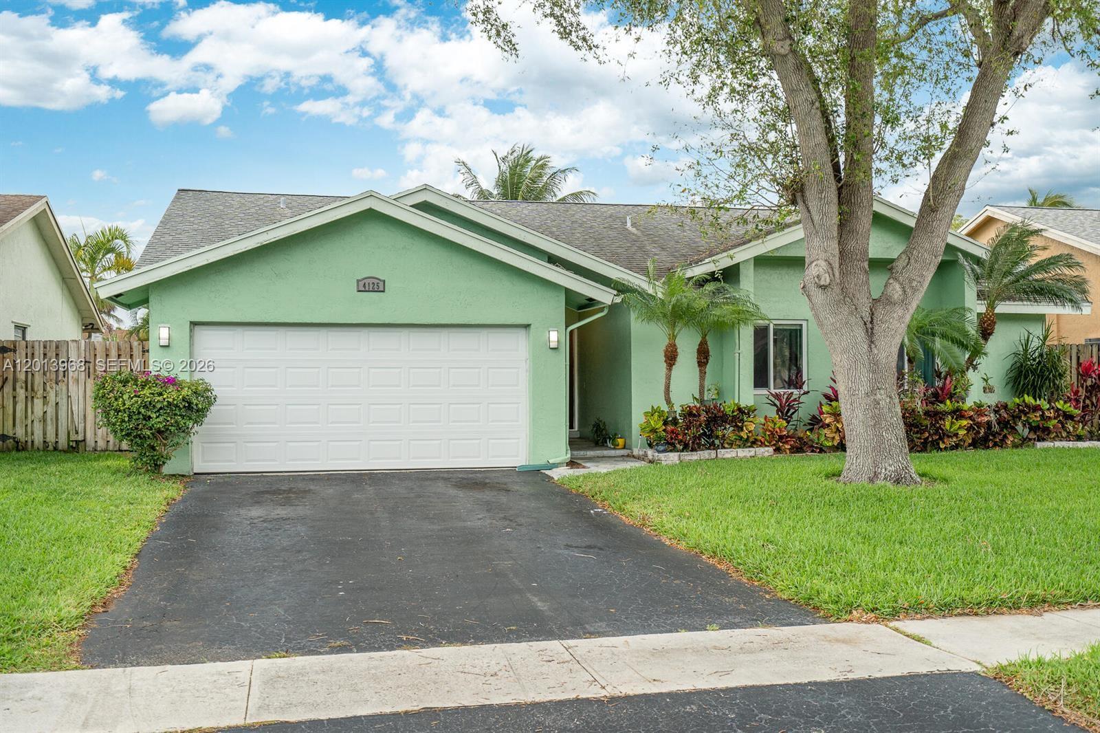 A light green single-story house features a two-car garage, a driveway, and mature landscaping — 4125 NW 96th Ter # 4125, Sunrise FL 33351, SUNRISE, FL