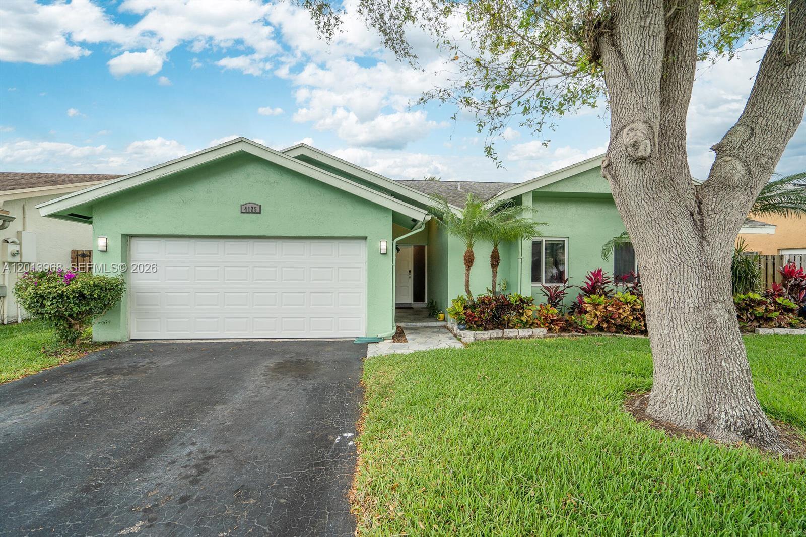 A single-story green house features a two-car garage, a paved walkway, and mature landscaping — 4125 NW 96th Ter # 4125, Sunrise FL 33351, SUNRISE, FL
