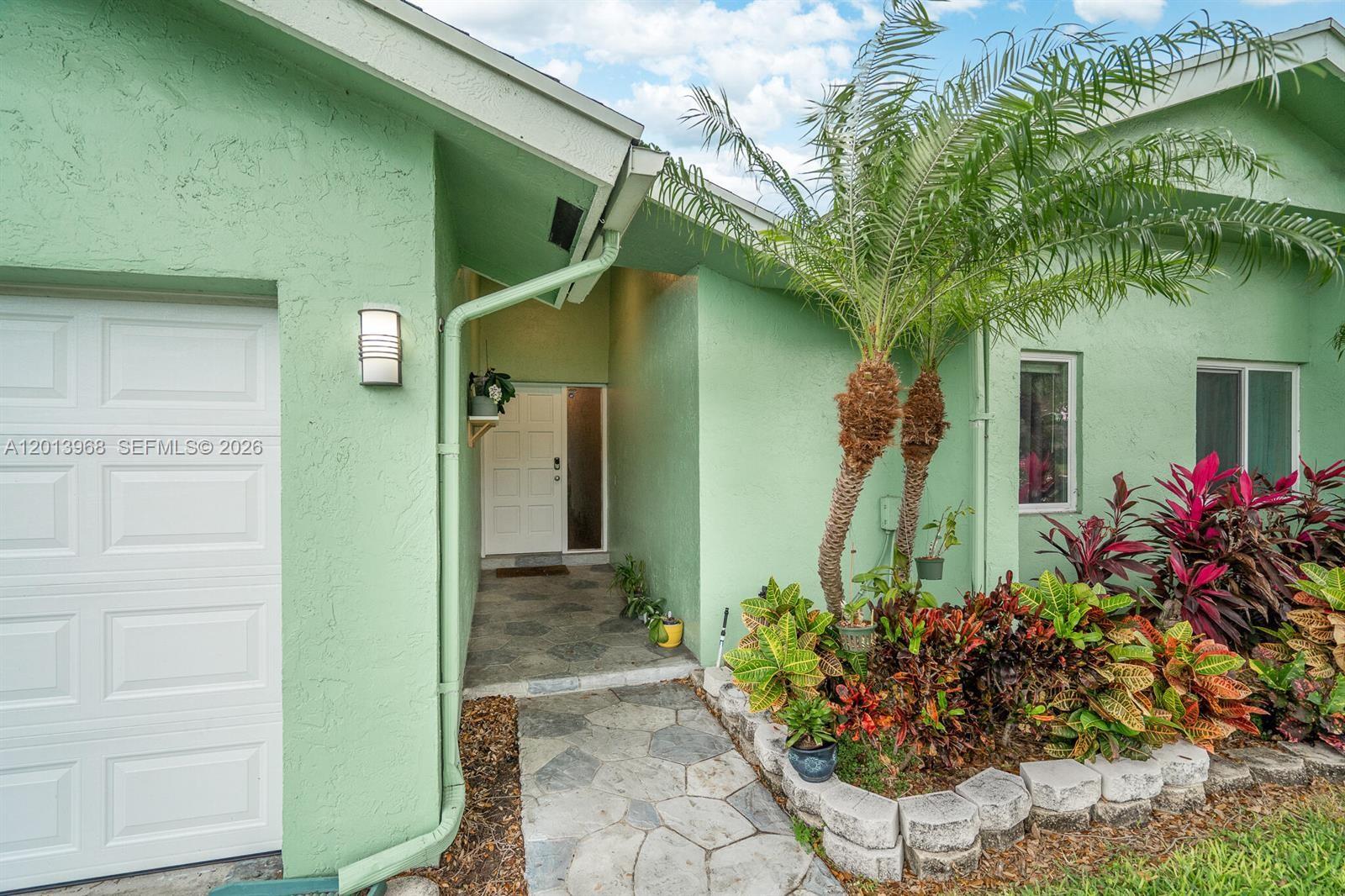 The exterior of a green house features a stone walkway, a palm tree, and landscaping — 4125 NW 96th Ter # 4125, Sunrise FL 33351, SUNRISE, FL