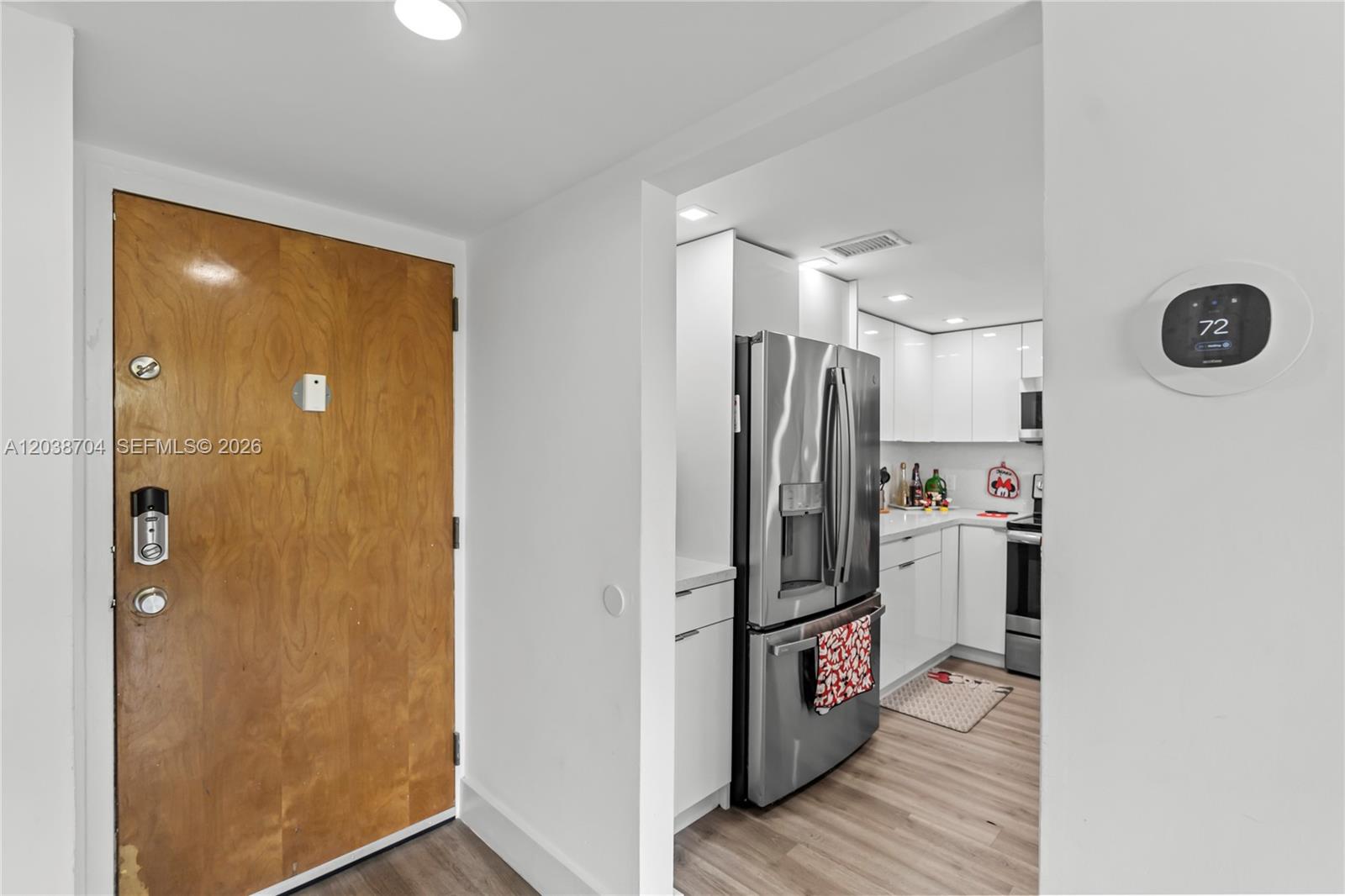A wooden front door opens into a kitchen featuring stainless steel appliances and white cabinetry — 2055 SW 122nd Ave # 326, Miami FL 33175, MIAMI, FL