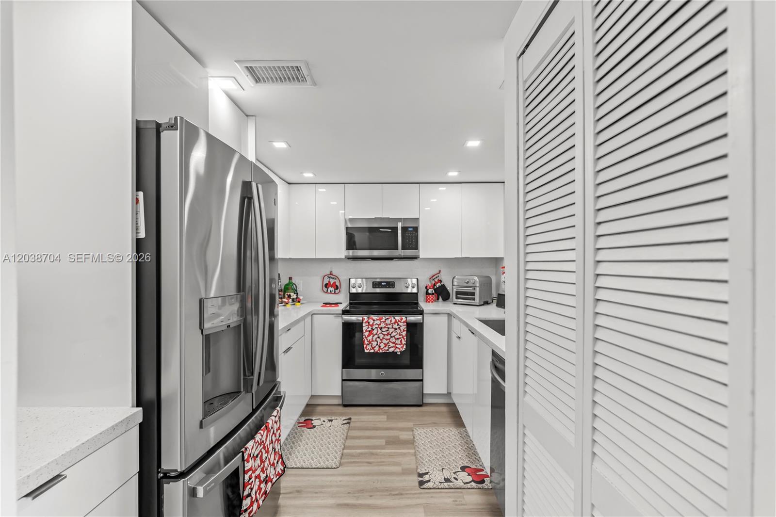 A modern galley kitchen features white cabinets, stainless steel appliances, and light wood-look flooring — 2055 SW 122nd Ave # 326, Miami FL 33175, MIAMI, FL