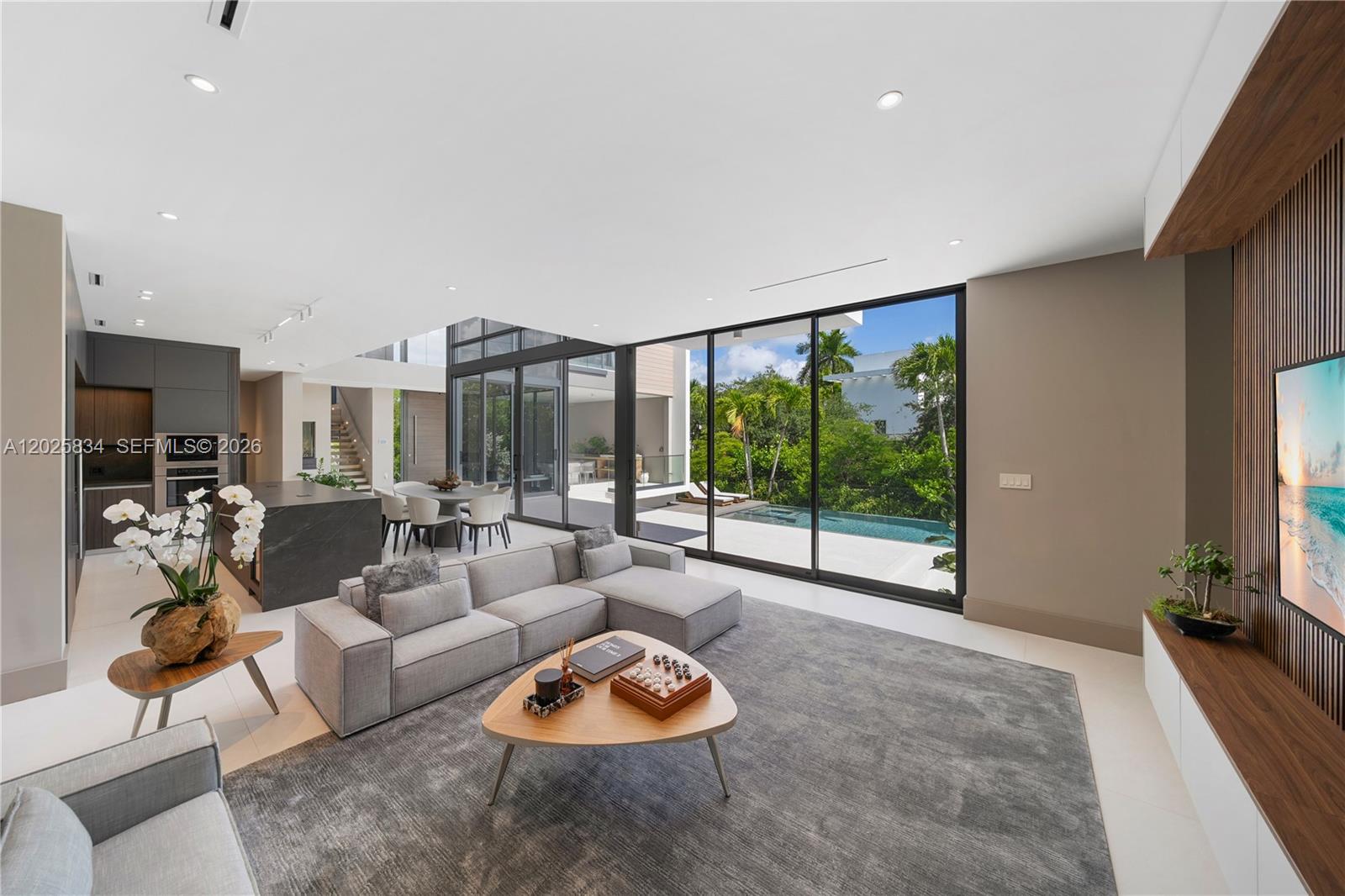 A modern living room features a gray sectional, triangular coffee table, and floor-to-ceiling glass doors — 571 Glenridge Rd, Key Biscayne FL 33149, KEY BISCAYNE, FL