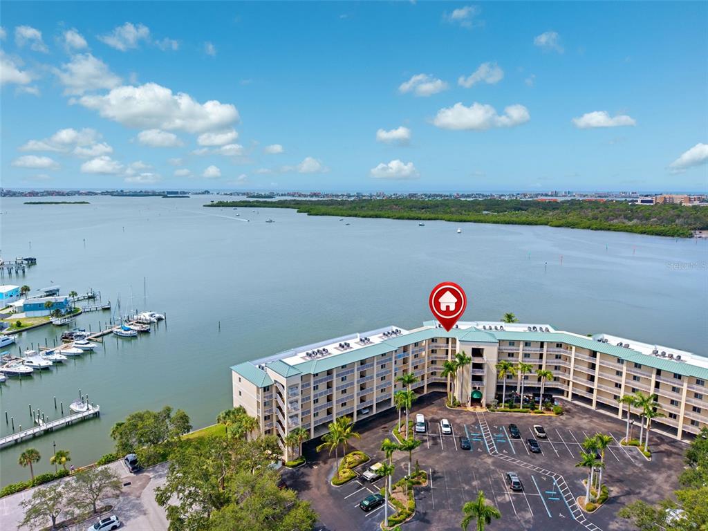 An aerial view shows a multi-story waterfront apartment building with a parking lot and boats — 8800 BAY PINES BOULEVARD UNIT 312, ST PETERSBURG, FL