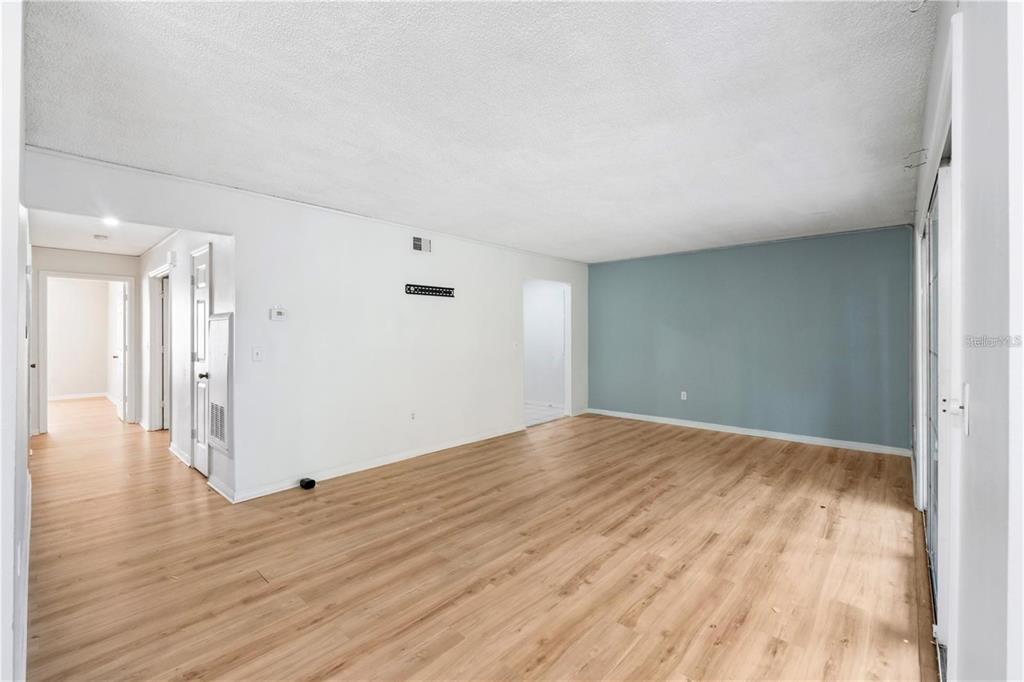An empty living room features light wood-look flooring, white walls, and one blue accent wall — 4160 VERSAILLES DRIVE UNIT 4160D, ORLANDO, FL