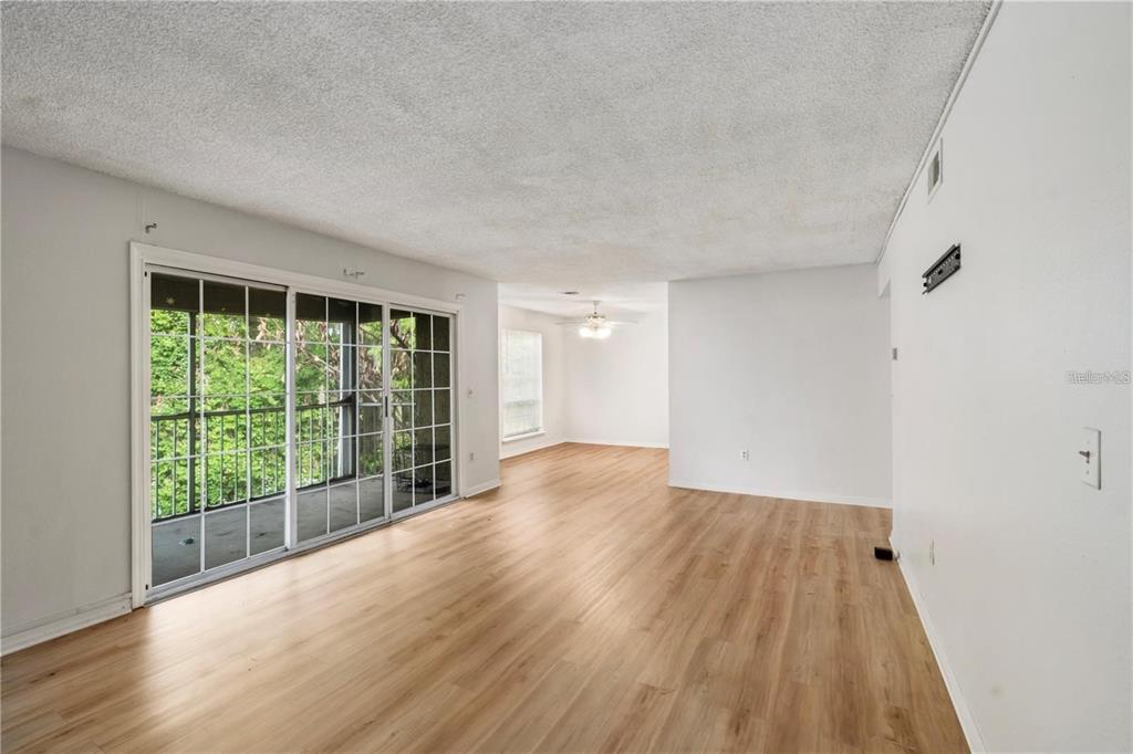 An empty living room with light wood-look flooring, white walls, and sliding glass balcony doors — 4160 VERSAILLES DRIVE UNIT 4160D, ORLANDO, FL