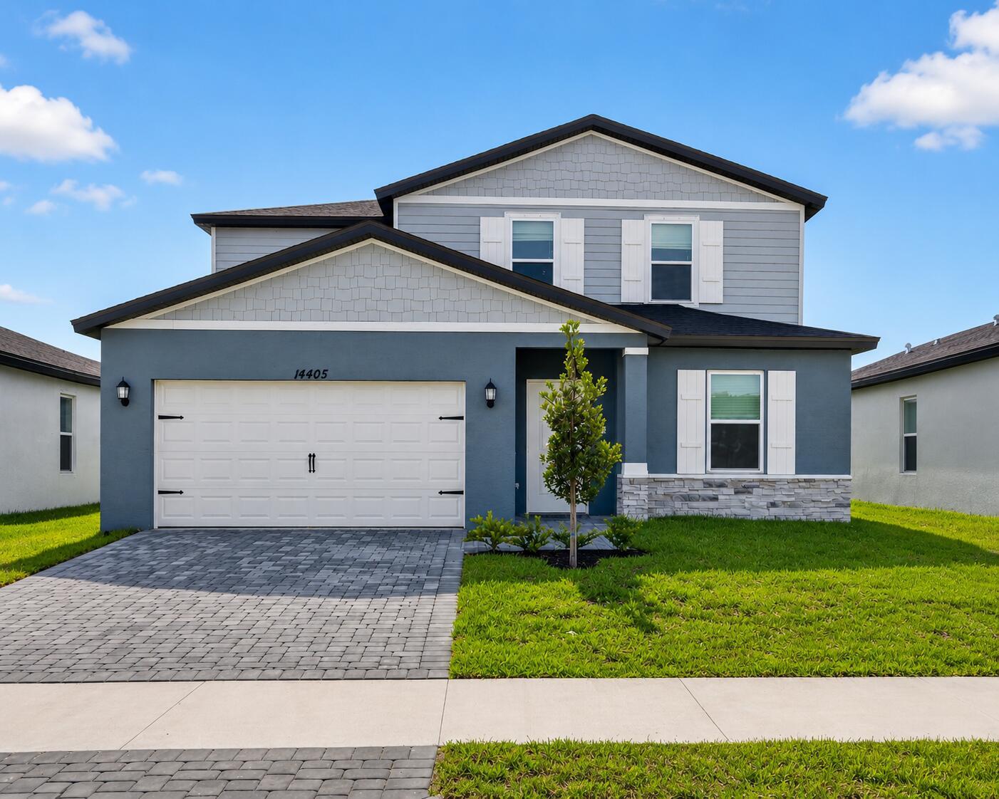 A two-story suburban house with a gray stucco exterior, stone accents, and a paved driveway — 14405 SW New Dawn Road, FL 34956, FL