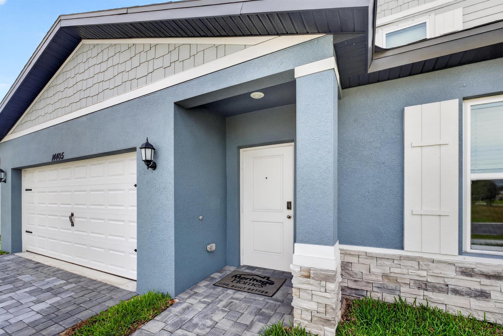 The exterior of a house features blue stucco walls, a white garage door, and stone accents — 14405 SW New Dawn Road, FL 34956, FL