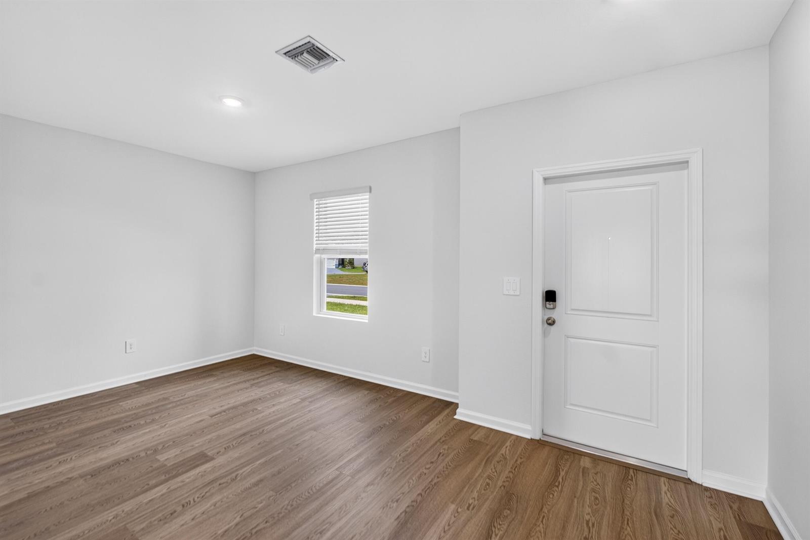 An empty room with light gray walls, wood-look flooring, a single window, and an entry door — 14405 SW New Dawn Road, FL 34956, FL