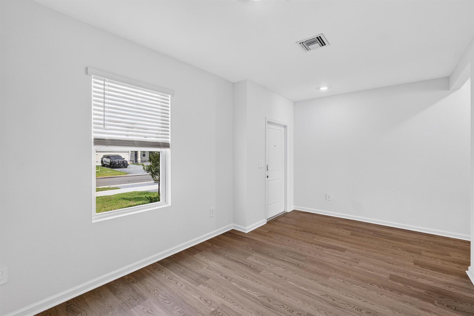 An empty room with white walls, wood-look flooring, a window with blinds, and a door — 14405 SW New Dawn Road, FL 34956, FL