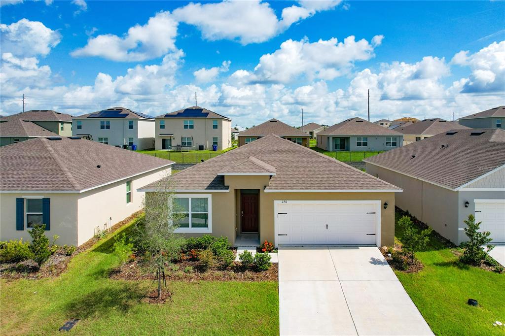 An exterior view of a single-story suburban house with a tan facade and two-car garage — 276 SOFIA LANE, LAKE ALFRED, FL