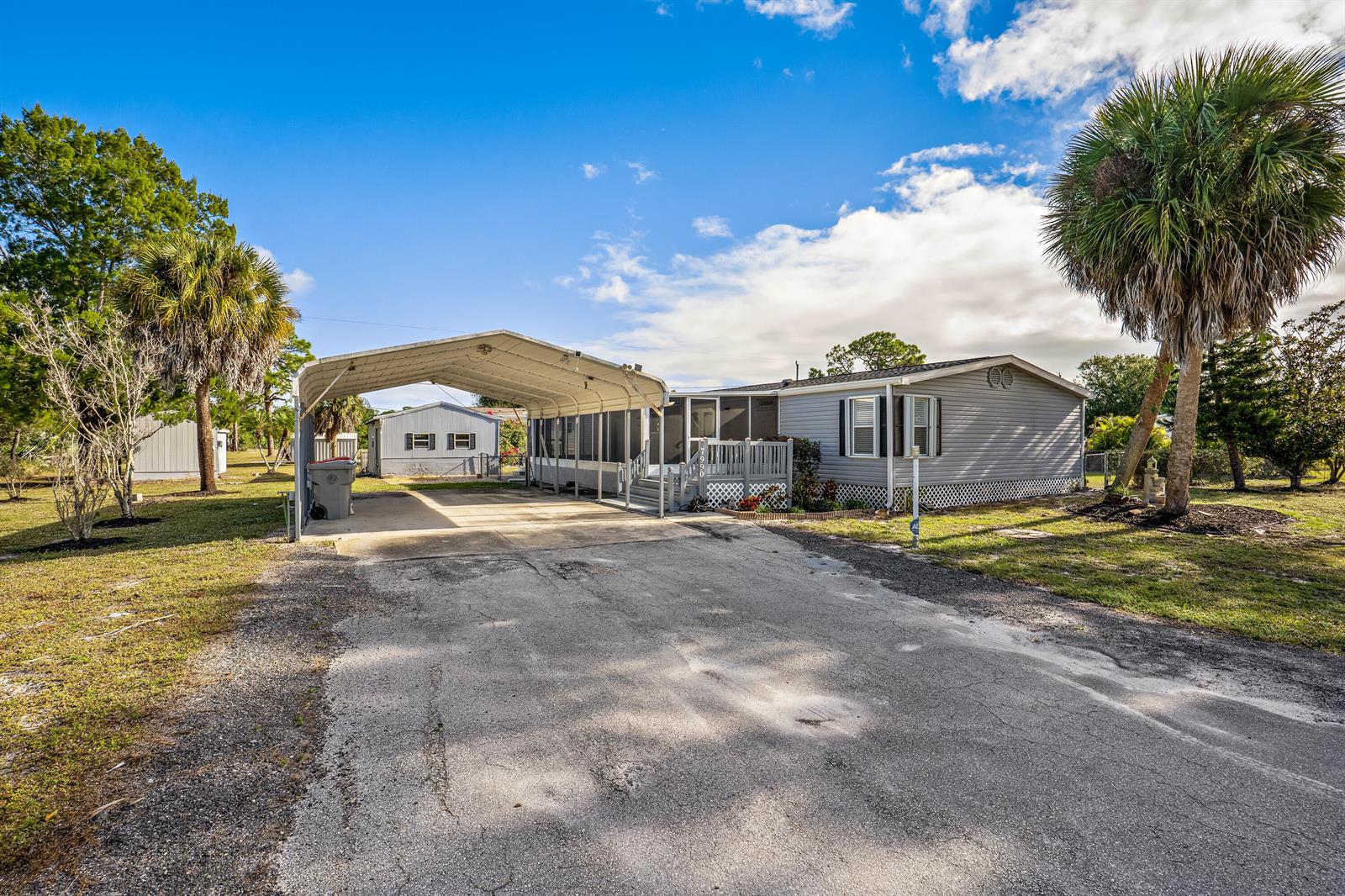 A gray manufactured home features a metal carport, a screened porch, and a paved driveway — 7990 129th Place, Sebastian FL 32958, SEBASTIAN, FL