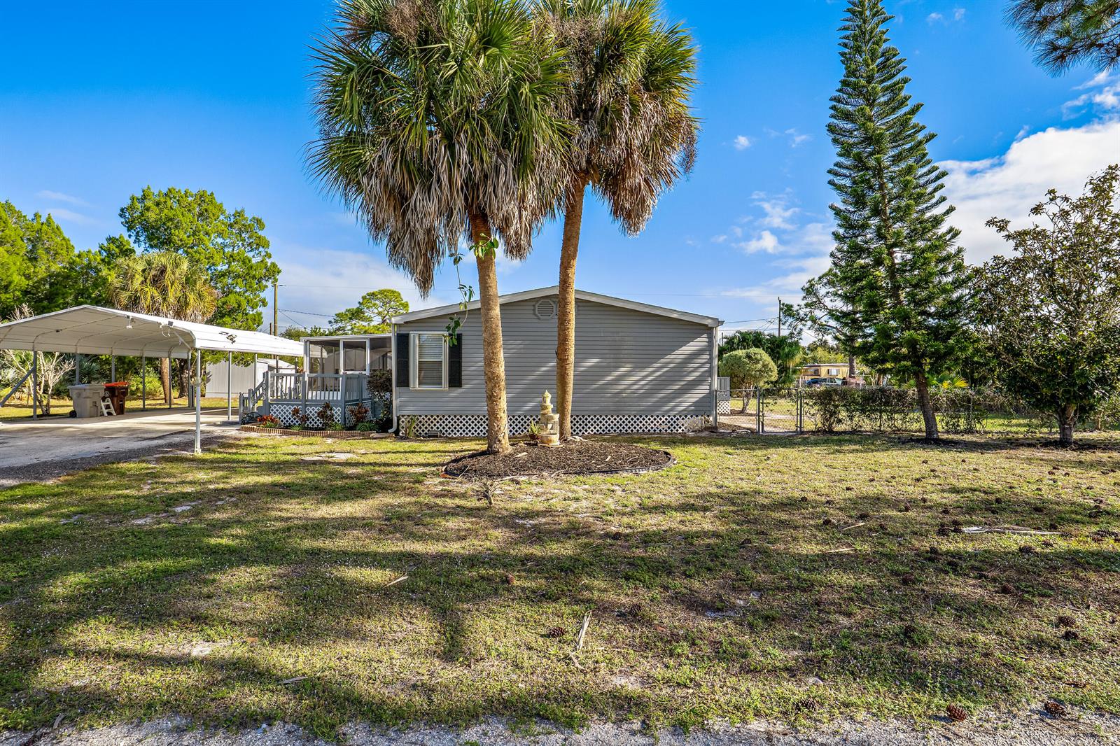 A gray mobile home features a carport, a screened porch, and two tall palm trees — 7990 129th Place, Sebastian FL 32958, SEBASTIAN, FL
