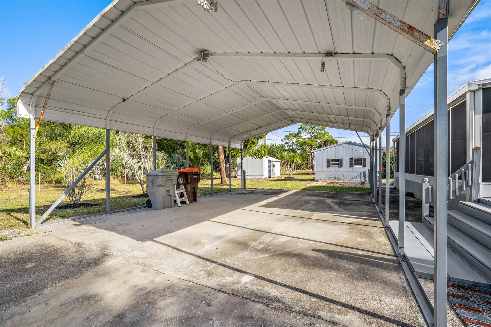 A concrete carport with a metal roof stands beside a house with stairs — 7990 129th Place, Sebastian FL 32958, SEBASTIAN, FL