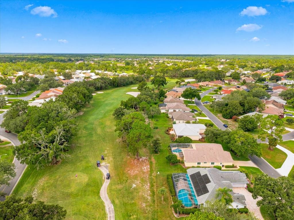 An aerial view shows a golf course fairway bordered by residential houses and a paved path — 9720 SOUTHERN BELLE DRIVE, WEEKI WACHEE, FL