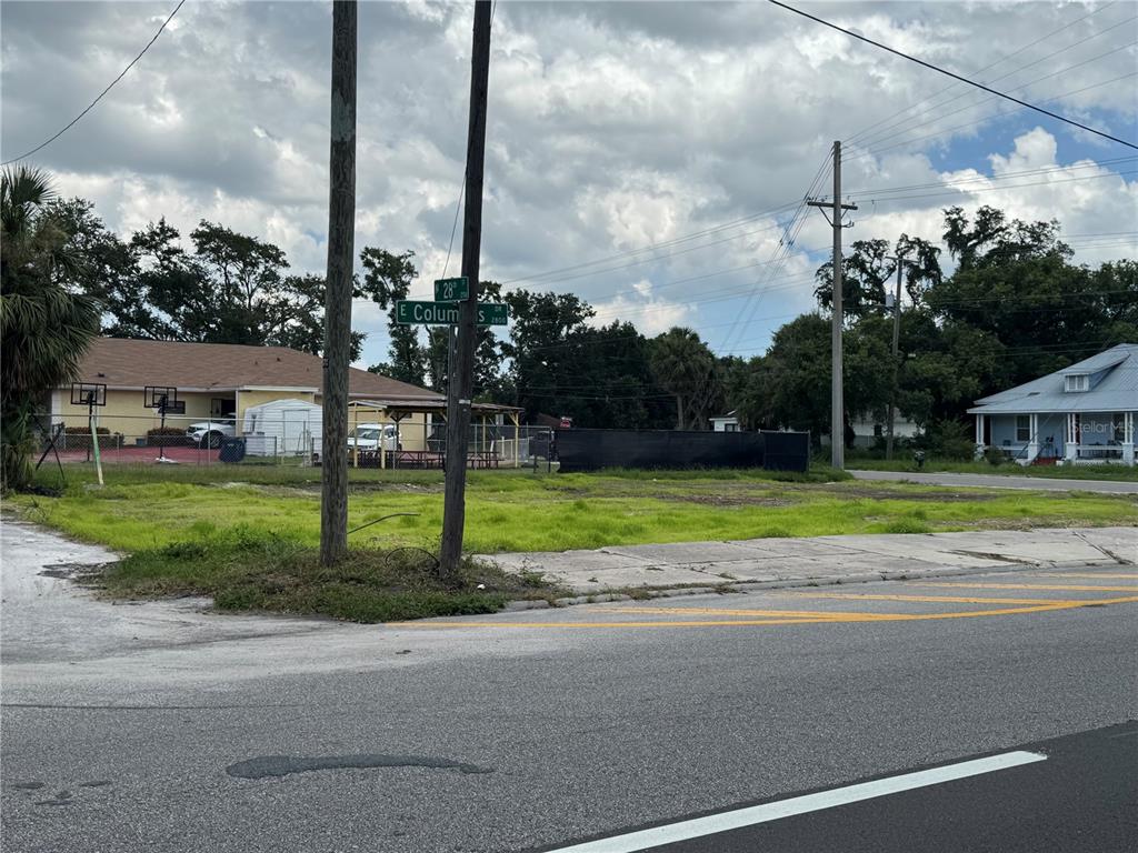 A vacant grassy lot sits at a street corner with utility poles and nearby houses — 2804 E COLUMBUS DRIVE, TAMPA, FL