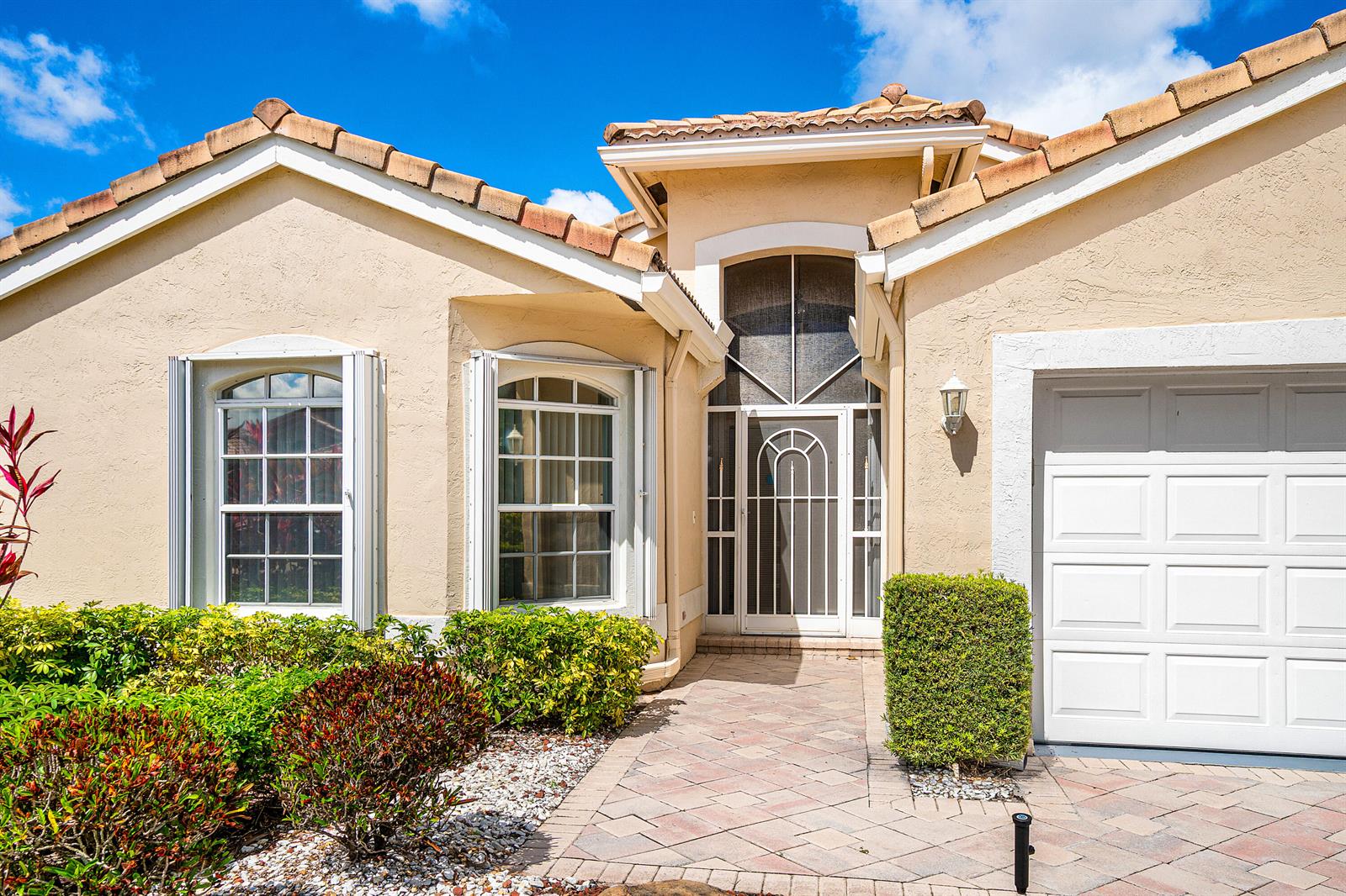 The exterior of a beige stucco house features a tiled roof, arched windows, and a garage — 6594 Sun River Road, Boynton Beach FL 33437, BOYNTON BEACH, FL