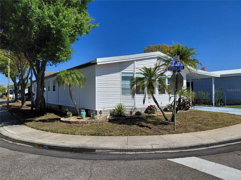 A white manufactured home sits on a corner lot with palm trees and landscaping — 1001 STARKEY ROAD UNIT 704, LARGO, FL