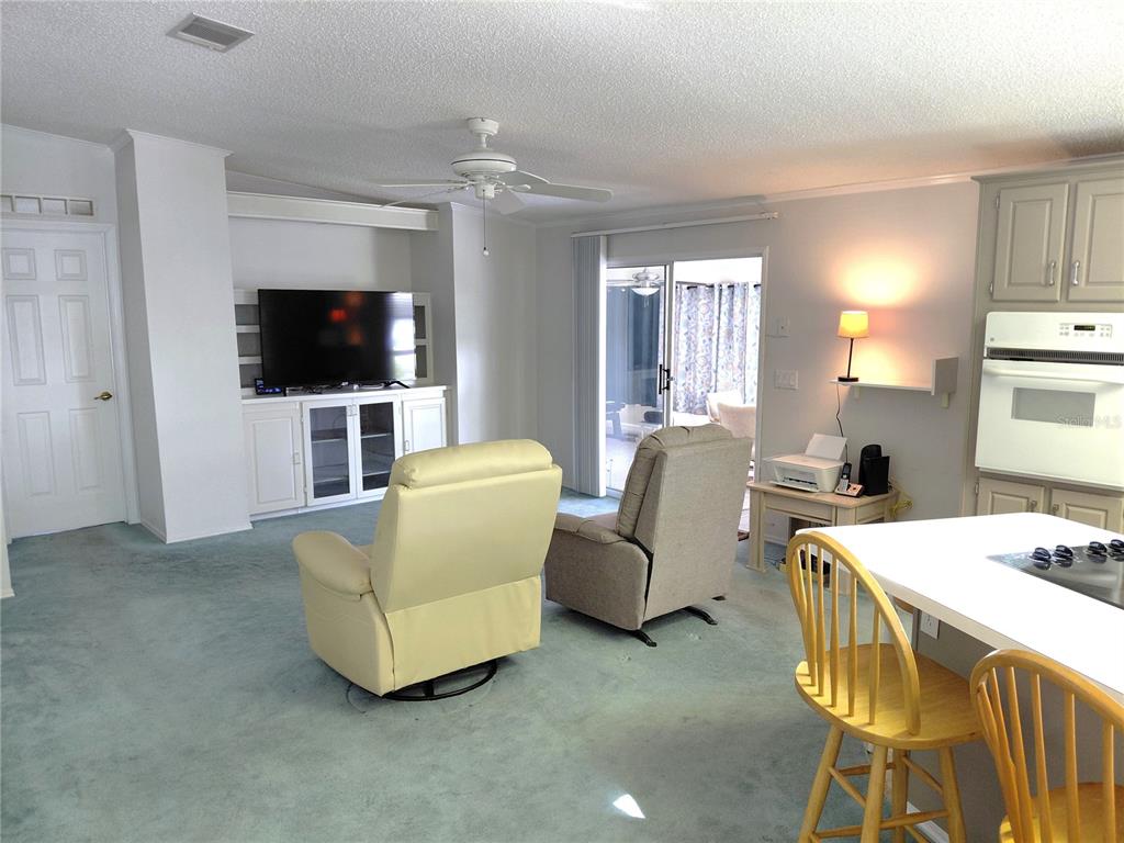 A living room with light blue carpet, two recliners, a television console, and kitchen seating — 1001 STARKEY ROAD UNIT 704, LARGO, FL