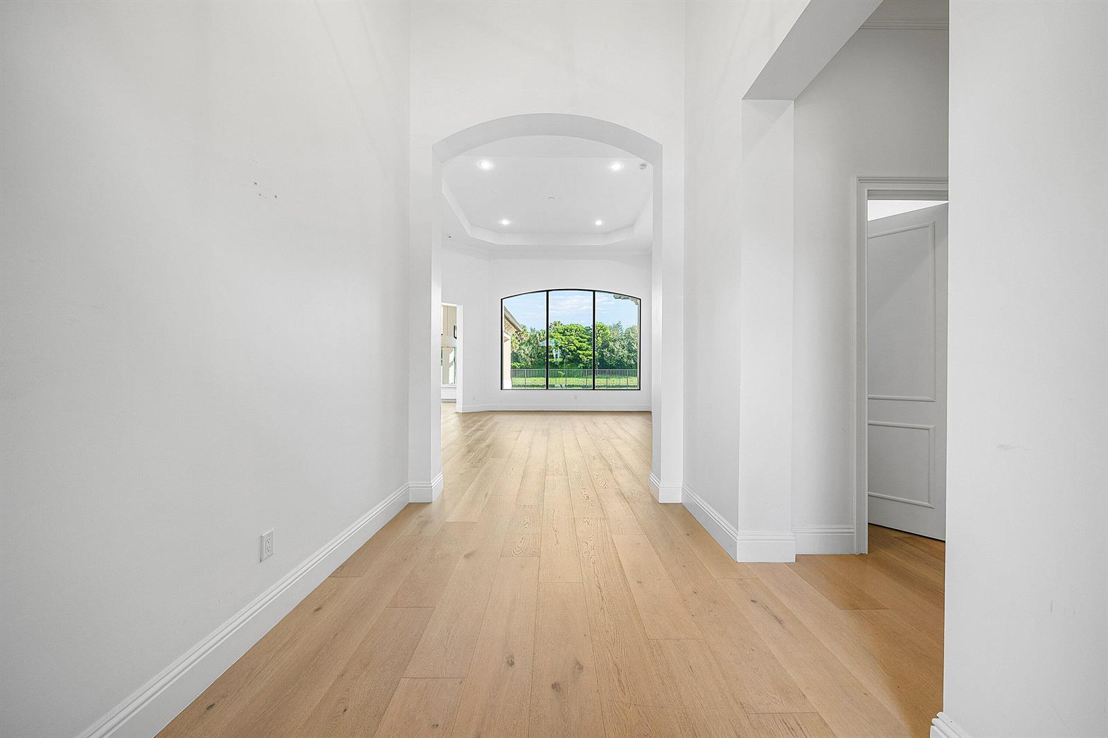 A bright, white hallway with light wood flooring leads to a room with large windows — 9599 Moritz Way, Delray Beach FL 33446, DELRAY BEACH, FL