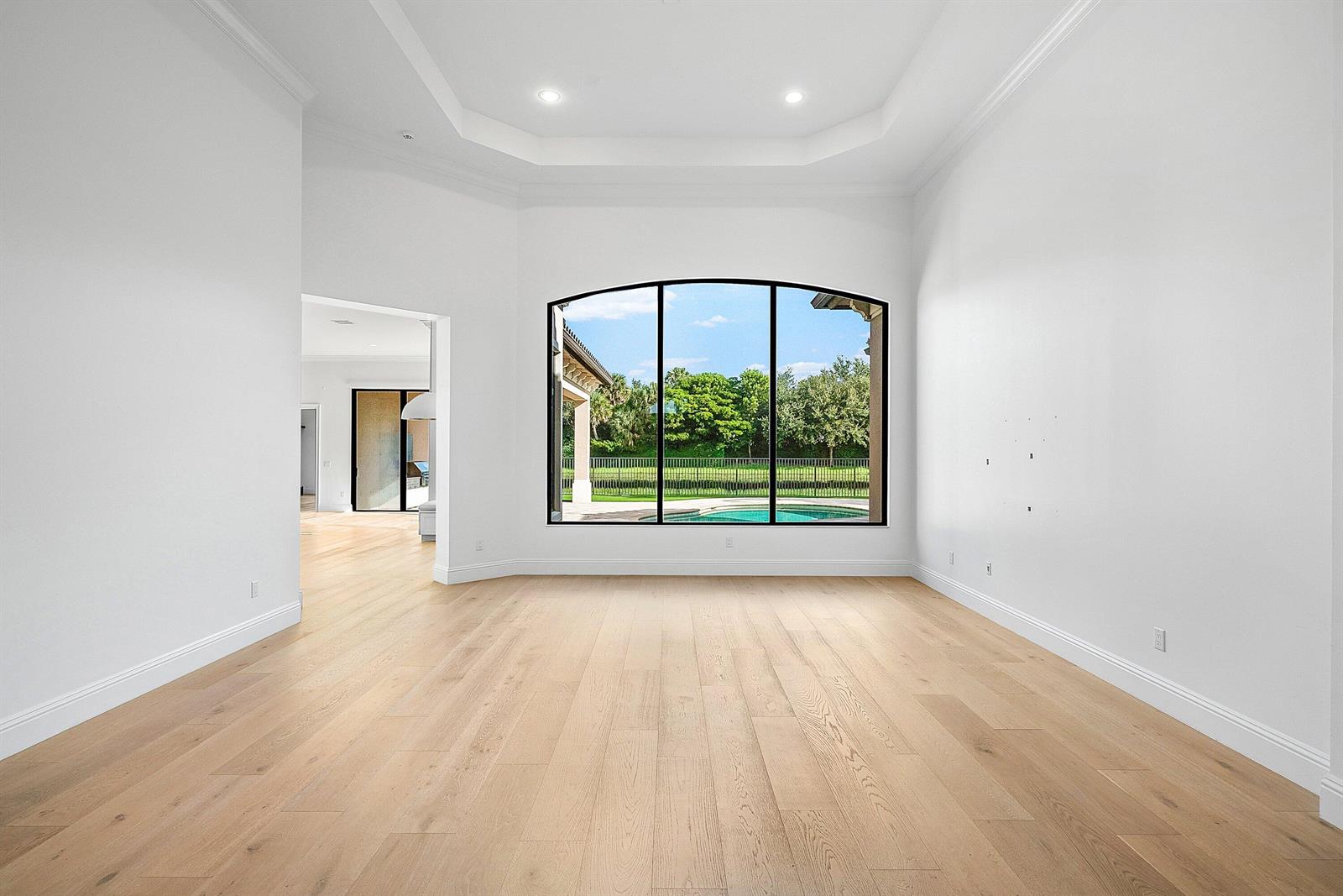 An empty room with light wood floors, white walls, a tray ceiling, and arched windows — 9599 Moritz Way, Delray Beach FL 33446, DELRAY BEACH, FL